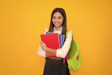 School teenage girl with school bag backpack hold book on yellow isolated studio background. Children school and education concept