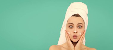 Cilt bakımlı güzel kadın. Şaşırmış genç kız mavi arka plana yüz kremi sürmüş. Güzel kadın, izole edilmiş yüz portresi, taklit alanı olan pankart.