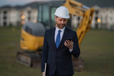 İnşaat mühendisi inşaat alanında çalışıyor. Evin arka planındaki mühendis. Modern ev inşaatında kendine güvenen mühendis. İspanyol inşaat mühendisi miğferinde