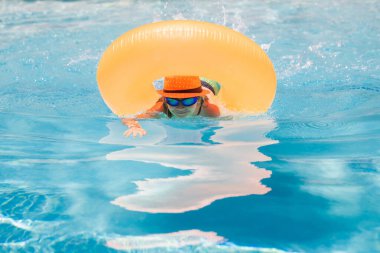 Child in swimming pool on inflatable ring. Kid swim with orange float. Water toy, healthy outdoor sport activity for children. Kids beach fun. Fashion summer kids
