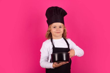 Aşçı çocuk tencereyle yemek yapıyor. Yemek pişirme, aşçılık ve çocuklar. Stüdyoda izole edilmiş şapka ve önlüklü küçük çocuk.