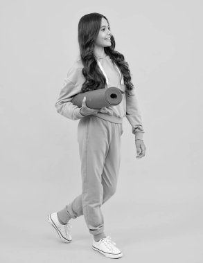 Child girl dressed in sports uniform. Child in a posh stylish sports suit in a hoodie with a hood hold yoga mat. Advertising sportswear tracksuit. Healthy kids lifestyle, sport
