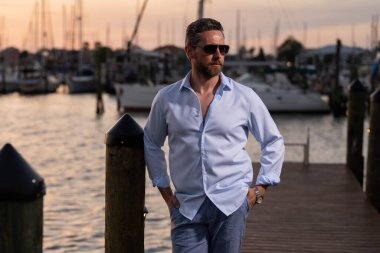 Yatın yanında hayal kuran ve düşünen zengin, şık bir iş adamı. Yat kulübünde kendine güvenen bir adamın portresi. Şık bir Lambersex modeli. Gömlek giymiş seksi bir adam. Moda erkeği yat yakınlarındaki marinada poz veriyor.