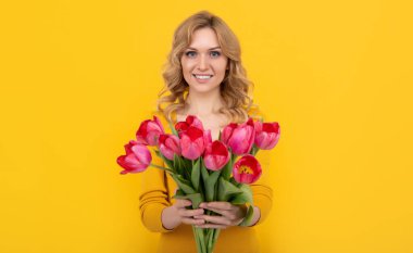 Sarı arka planda bahar lale çiçekleri olan mutlu, güzel bir kadın..