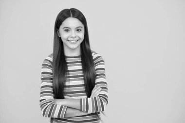 Happy face, positive and smiling emotions of teenager girl. Copy space. Cute little teenager girl crossing arms over yellow background
