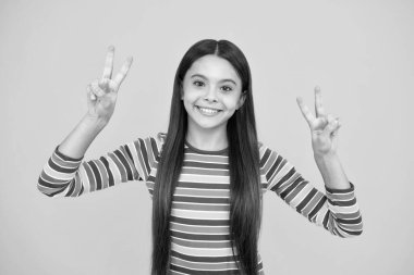 Mutlu yüz, pozitif ve gülümseyen genç kız duyguları. 12, 13, 14 yaşlarında genç bir çocuk zafer işareti gösteriyor. İkincisi, sarı arkaplanda izole edilmiş V işareti.