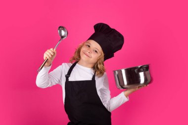 Çocuk aşçı tencere ve kepçeyle yemek pişirir. Yemek pişiren çocuklar. Aşçı bozuntusu aşçı. Önlüklü ve aşçı şapkalı çocuk mutfakta sağlıklı bir yemek hazırlıyor. Yemek pişirme süreci