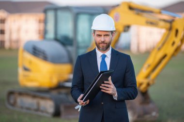Takım elbiseli ve kasklı bir Buider. İnşaat yatırımcısı. İnşaat alanının önündeki yatırımcı. Başarılı bir yatırımcı. İnşaatta takım elbiseli yakışıklı ve kasklı bir adam.
