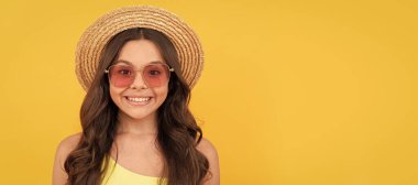 happy kid in summer straw hat and glasses has curly hair on yellow background, summer mood. Child face, horizontal poster, teenager girl isolated portrait, banner with copy space
