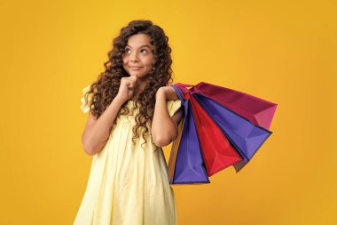 Sarı arka planda alışveriş torbaları olan güzel moda kızı. Alışveriş ve moda alışverişi. Alışveriş çantalı çocuk. Düşünen yüz, genç kızın düşünceli duyguları.