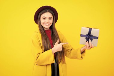 Mutlu ergen portresi. Gülümseyen kız. Sarı izole edilmiş arka planda hediye kutusu tutan ergen bir çocuk. Çocukların doğum günü hediyesi. Sonbahar tatili