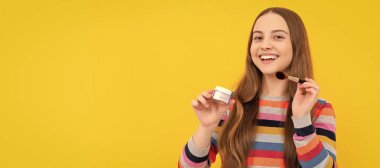 Cute makeup artist. Happy girl apply makeup. Child smile using foundation brush. Beauty and visage. Cosmetics for teenager child, poster design. Beauty kids makeup, banner with copy space