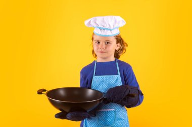 Çocuk aşçı tavayla yemek pişirir. Aşçı bozuntusu aşçı. Önlüklü ve aşçı şapkalı çocuk mutfakta sağlıklı bir yemek hazırlıyor. Yemek pişirme süreci