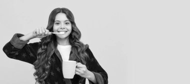 Rahat bornozlu mutlu kız çocuğu diş fırçası, bardak ve kişisel bakım kullanın. Diş fırçası, stüdyo resmi, fotokopi alanı ile başlık