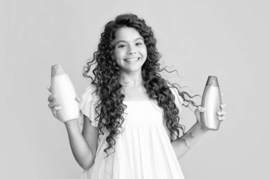 Şampuan kremi ve duş jeli olan genç bir kız. Genç kızın uzun saçı. Kozmetik ürünler, şampuan şişesi. Heyecanlı bir genç, şaşkın ve neşeli duygular içinde