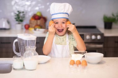 Çocuk aşçı yumurtalarla yemek yapıyor. Komik aşçı çocuk mutfakta aşçılık yapıyor. Aşçı çocuk sağlıklı yemek yapıyor. Şef şapkalı küçük çocuğun portresi.