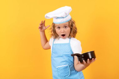 Mutfak saksısı olan komik aşçı çocuk. Yemek pişiren çocuklar. Aşçı bozuntusu aşçı. Önlüklü ve aşçı şapkalı çocuk mutfakta sağlıklı bir yemek hazırlıyor. Yemek pişirme süreci