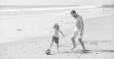 Baba ve çocuk dışarıda eğleniyorlar. Çocukluk ve ebeveynlik. Aile tatilleri. Spor aktivitesi. Baba ve oğul plajda futbol oynuyorlar. Güneşli yaz gününde babasıyla küçük oğlu. hafta sonu aile günü.