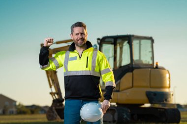 Worker with bulldozer on site construction. Man excavator worker. Construction driver worker with excavator on the background. Construction worker with tractor or construction vehicle at building