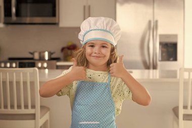 Portrait of funny child chef in kitchen. Chef kid cook baking at home kitchen. Kid chef cook cookery at kitchen. Cooking, culinary and kids. Little boy in chefs hat and apron