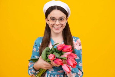Happy teen girl in hat hold spring tulip flowers on yellow background