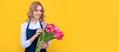 Sarı arka planda bahar lale çiçekleri olan önlüklü genç bir kadın. İzole edilmiş yüz portresi, taklit alanı olan pankart