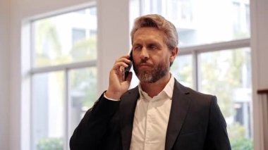Takım elbiseli bir adam telefonda konuşuyor. Olgun, telefonlu, heyecanlı bir İspanyol iş adamı. İş iletişimi. Müzakere çevrimiçi. Ofiste iş adamı telefonda konuşuyor. Telefon kullanan bir iş adamı.