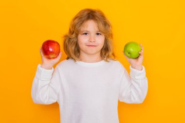 Kids face with fruits. Kid with apple in studio. Studio portrait of cute child hold apple isolated on yellow background