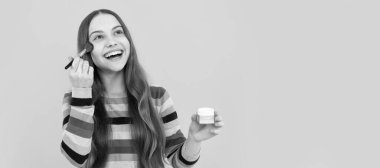 Mutlu çocuk makyaj malzemelerini toz fırçası sarı arka planda kullanıyor. Genç çocuklar için makyaj malzemeleri, poster tasarımı. Güzellik çocukları makyaj, fotokopi alanı ile pankart