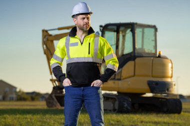 İnşaat işçisi endüstriyel alanda kazıcı ile çalışıyor. Kask takan, buldozerli bir işçi. Mühendis, inşaat firmasında çalışıyor. Traktörlü kazı ustabaşı