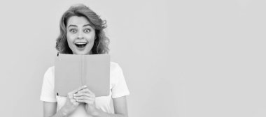 Şaşırmış bir kız sarı arka plan ve okul defterini tutuyor. İzole edilmiş yüz portresi, kopyalama alanı olan pankart