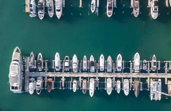 Miami marinası boyunca lüks bir yat ve tekne manzarası. Turkuaz tropikal sularda beyaz bir yatın hava görüntüsü. Seçkin bir yat. Canlı bir marinada yatlar. Lüks yatlar gezisi