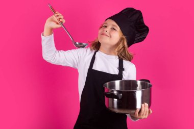 Çocuk tencere ve kepçeyle yemek pişiriyor. Heyecanlı aşçı şefi. Çocuk fırın üniforması ve aşçı şapkası giyiyor yemek hazırlıyor, stüdyo fotoğrafı çekiyor.