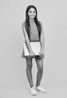 Sarı arka planda izole edilmiş günlük kıyafetlerle dizüstü bilgisayarı olan zeki kız.