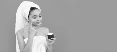 pretty kid in bath tower applying skin cream, healthy skin. Cosmetics and skin care for teenager child, poster design. Beauty kid girl banner with copy space