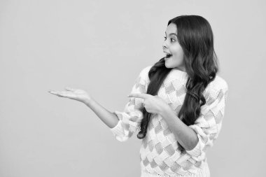 Onun yakın plan portresi. Güzel, çekici, neşeli, şaşkın kız, sarı arka planda izole edilmiş fotokopi alanını işaret ediyor. Kopyalama alanını düzenle