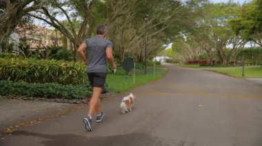 Sporcu koşuyor, yavaş çekimde. Sabah sporu rutini. İnsan ve köpek koşuyor. Açık hava yürüyüşü. Sporcu adam antrenman için koşuyor. Sporcu adam koşusu. Koşucu köpeğiyle koşuyor..