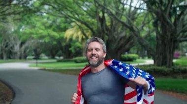 Spor maratonu koşusu. Amerikan bayrağı adamın elinde. 4 Temmuz. Spor koşusunda Amerikan bayrağı taşıyan bir koşucu. Erkek koşucu dışarıda koşuyor. Bağımsızlık Günü. Vatansever adam koşuyor. Amerikan bağımsızlığı.