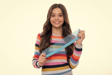 Sarı izole edilmiş stüdyo arka planında saçlarını tarayan bir genç. Saç fırçası olan genç bir kız. Çocukların saç stili. Mutlu kız yüzü, pozitif ve gülümseyen duygular