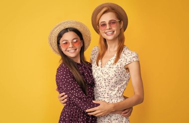 Sarı arka planda hasır şapkalı neşeli anne ve kız.