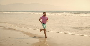 Sahilde koşan sağlıklı bir adam. Enerjik bir yaz. Koşucu özgürlüğü hisseder. Sabahın tadını çıkarıyorum. Dayanıklılık ve dayanıklılık. Spor atleti okyanusta hızlı koşar. sabah çalışma aktivitesi.