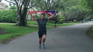 Spor koşusunda Amerikan bayrağı taşıyan bir koşucu. Erkek koşucu dışarıda koşuyor. Bağımsızlık Günü. Vatansever adam koşuyor. Amerikan bağımsızlığı. Spor maratonu koşusu. Amerikan bayrağı adamın elinde. Ulusal bayrak.