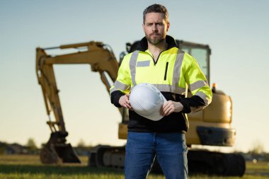 İnşaat alanındaki bir inşaatçının portresi. Kazıcı yeni bir ev inşa etmeye hazır. İnşaat işçileri kazı kamyonu kazılarında inşaat üniforması giyerler, inşaat işlerinde çalışırlar.