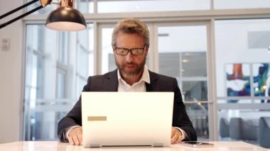 Ofiste dizüstü bilgisayar kullanan bir adam. Serbest iş yapma. Erkek ofis yöneticisi. İş adamının internet işi var. İş adamı başarıdan memnun. Serbest çalışan adam internette çalışıyor. Çevrimiçi çalışan serbest çalışan.