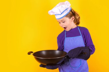 Çocuk aşçı tavayla yemek pişirir. Çocuk aşçı, stüdyo resmi. Çocuklar yemek yapıyor. Önlüklü ve aşçı şapkalı genç çocuk.