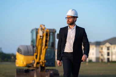 Takım elbiseli ve kasklı bir Buider. İnşaat yatırımcısı. İnşaat alanının önündeki yatırımcı. Başarılı bir yatırımcı. İnşaatta takım elbiseli yakışıklı ve kasklı bir adam.