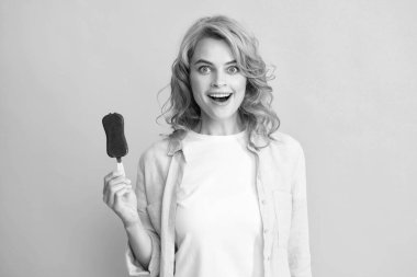 Genç bir kadının lezzetli dondurmalar yediği, dondurulmuş tatlılardan hoşlandığı, günlük kıyafetler giydiği, sarı arka planda izole edilmiş bir fotoğraf. Şaşırmış kadın yüzü