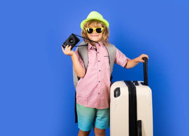 Stüdyoda seyahat çantası taşıyan bir çocuk gezgini. Çocuk turizmi