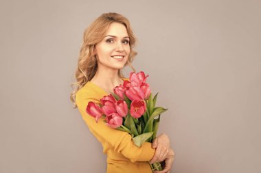 smiling woman with tulips. lady hold flowers for spring holiday. girl with bouquet on grey background. floral present for womens day. 8 march and mothers day.