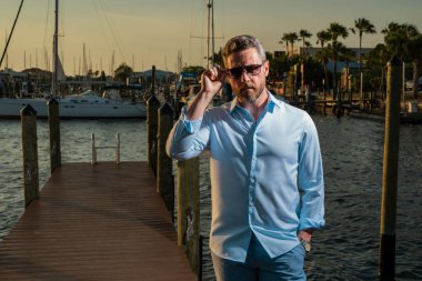 40 'lı yılların adamı yatın yanında. Dışarıdaki mankenin portresi. Moda erkeği yatların yanında poz veriyor. Şehir tarzında bir moda adamı. Yat kulübündeki yakışıklı İspanyol adam. Lüks yatın yanındaki körfezdeki adam.